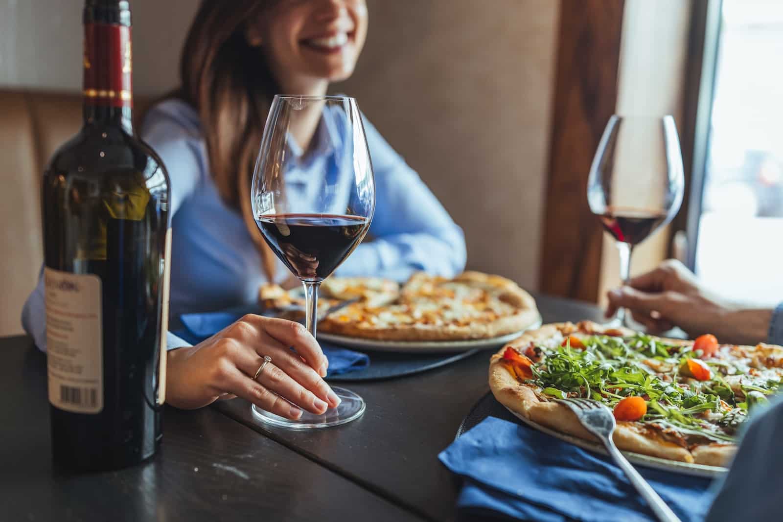Romantic Things to Do in Wausau, Wisconsin: A Date Night Guide 1 A couple enjoys wood-fired pizza and red wine at a cozy restaurant table, one of the romantic things to do in Wausau, WI.